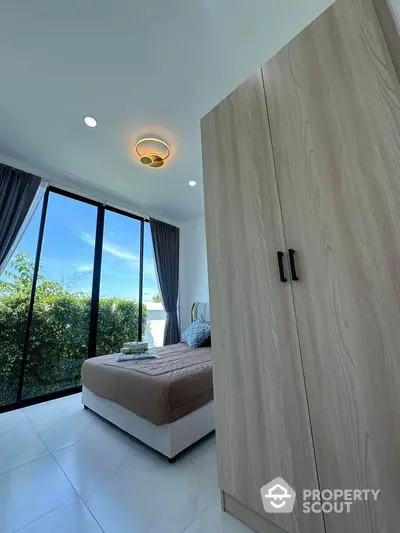 Modern bedroom with large window and stylish wardrobe, offering serene garden views.