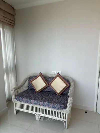 Cozy corner with wicker loveseat and decorative pillows in a bright room, perfect for relaxation.