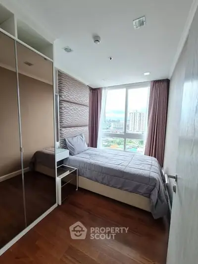Modern bedroom with large window offering city view, mirrored closet, and stylish decor.