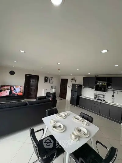 Modern open-layout living room with sleek kitchen and dining area, featuring stylish black furniture and bright lighting.