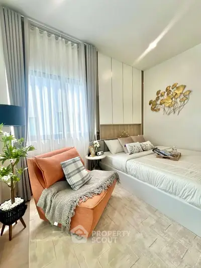 Cozy bedroom with modern decor and natural light, featuring a stylish armchair and elegant wall art.