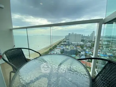 Stunning ocean view from high-rise balcony with glass railing and outdoor seating.