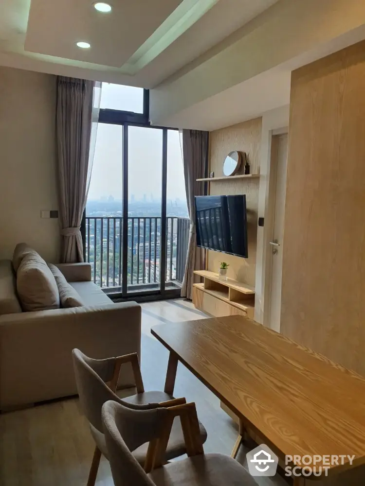 Cozy living room with modern furniture, large windows offering a stunning city view, and access to a spacious balcony, perfect for urban living.