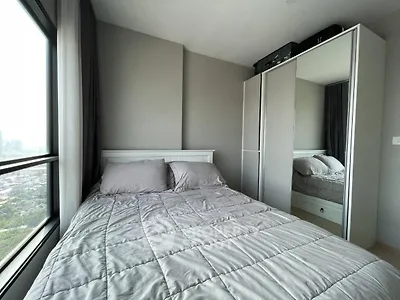 Modern bedroom with large window and mirrored wardrobe offering city views.
