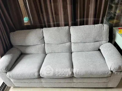 Cozy gray sofa in a modern living room with floor-to-ceiling windows and elegant curtains.