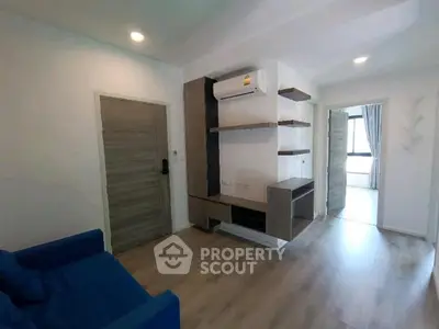 Modern living room with sleek wooden flooring and built-in shelving, featuring a cozy blue sofa and air conditioning.