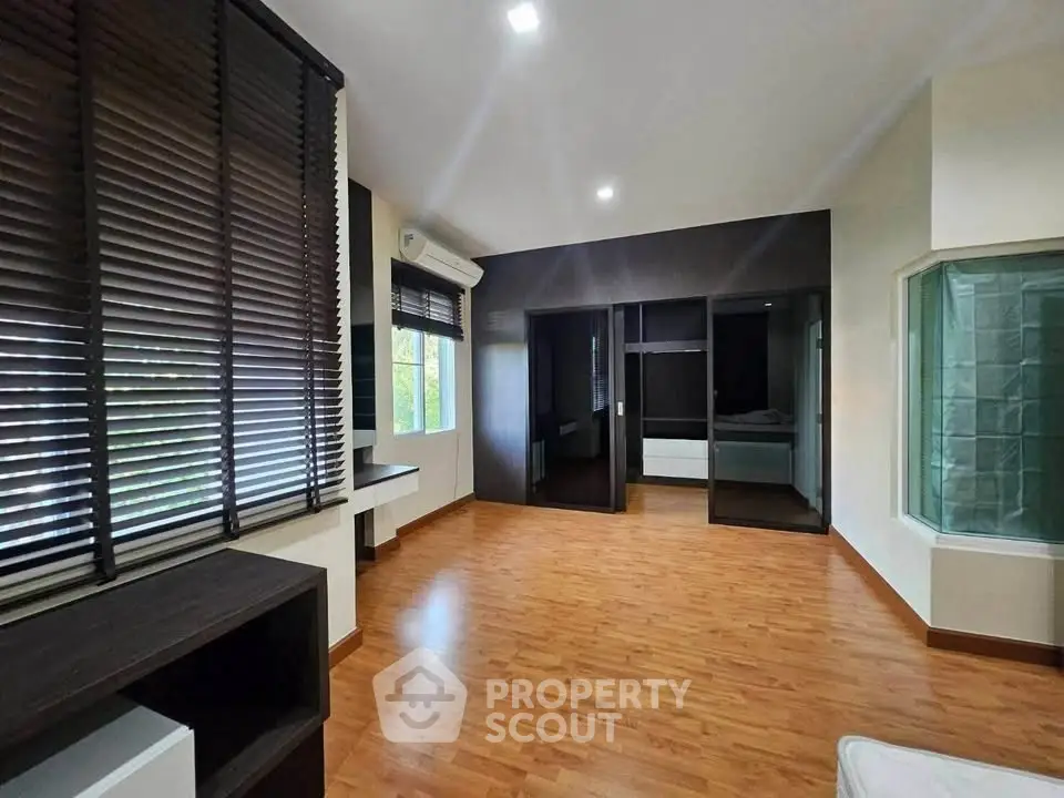 Spacious bedroom with wooden flooring and large windows for natural light.