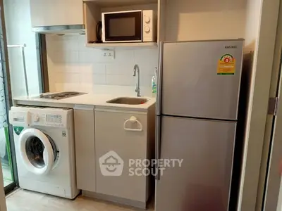 Compact kitchen with modern appliances including fridge, microwave, and washing machine in a cozy apartment.