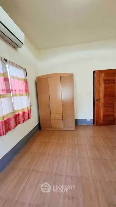 Spacious bedroom with wooden wardrobe and air conditioning, featuring tiled flooring and colorful curtains.