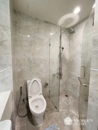 Modern bathroom with marble tiles featuring a glass shower enclosure, sleek fixtures, and a well-lit ambiance perfect for urban living.