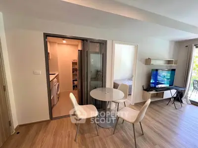 Modern apartment interior with open living area, dining set, and visible bedroom and laundry room.