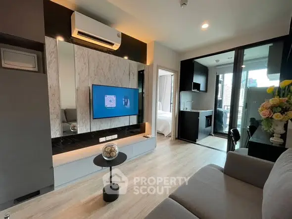 Modern living room with sleek design, featuring a wall-mounted TV, air conditioning, and access to a compact kitchen.