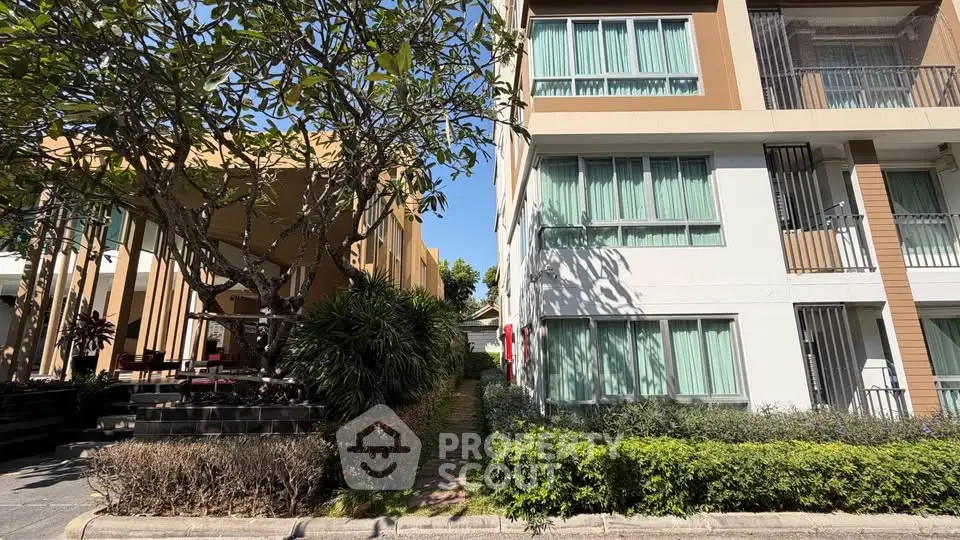 Modern apartment building exterior with lush greenery and clear blue sky.