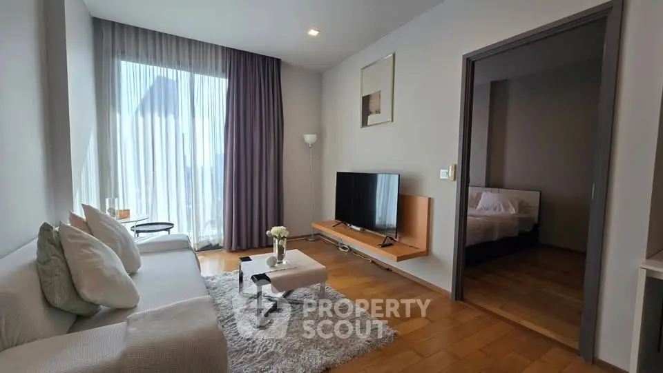 Modern living room with cozy decor and natural light, featuring a TV and access to a bedroom.