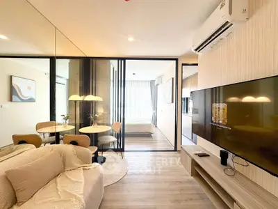 Modern open-plan living room with stylish decor and glass partition leading to a cozy bedroom.