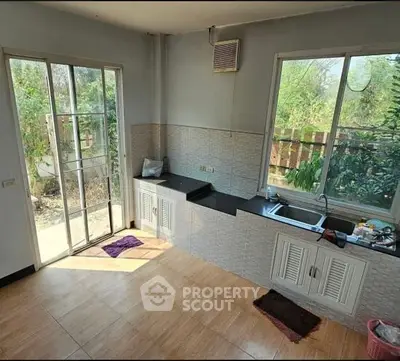 Bright kitchen with large windows and garden view, featuring sleek countertops and tiled flooring.