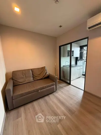 Cozy living room with modern sofa and view into sleek kitchen with glass partition.