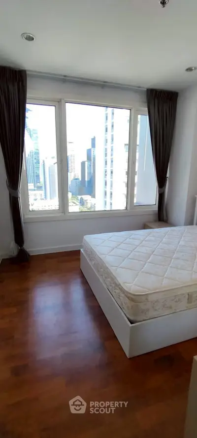 Spacious bedroom with large windows offering stunning city views and natural light.