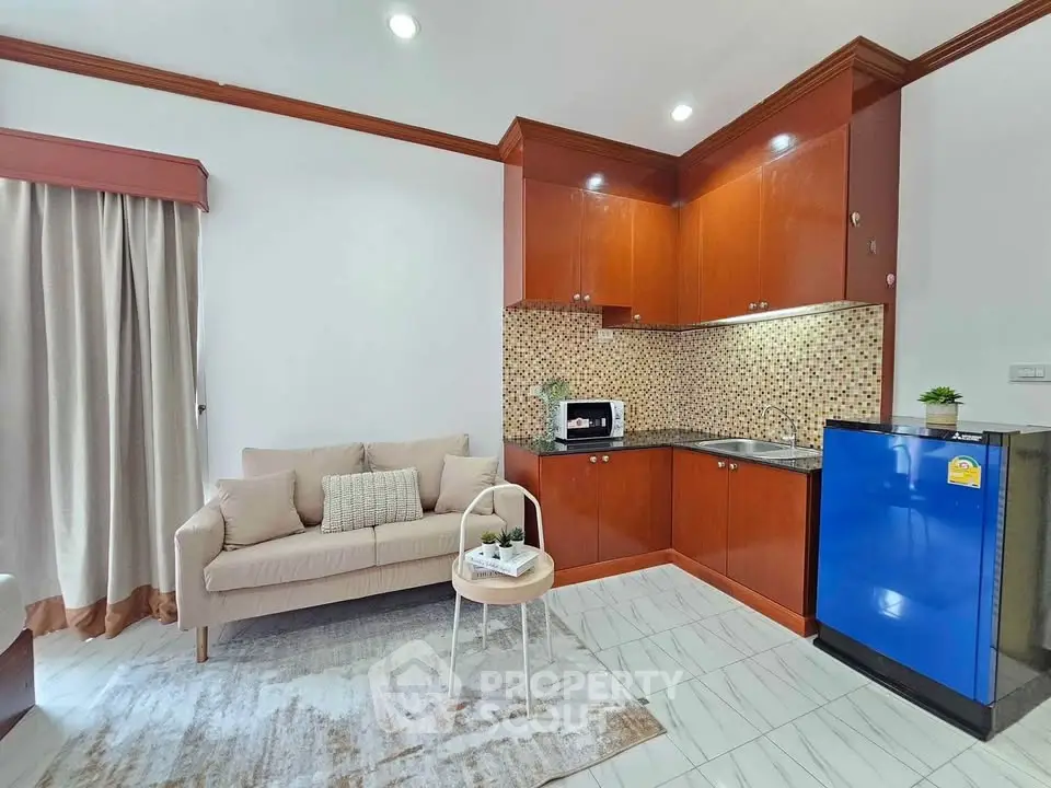 Charming living room with cozy sofa and modern kitchen featuring sleek cabinetry and vibrant blue fridge.