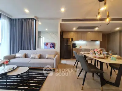 Modern open-layout living room with stylish kitchen and dining area, featuring elegant lighting and cozy decor.