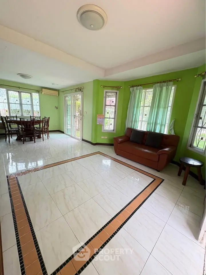Spacious living room with tiled flooring and green walls, featuring a cozy sofa and dining area.
