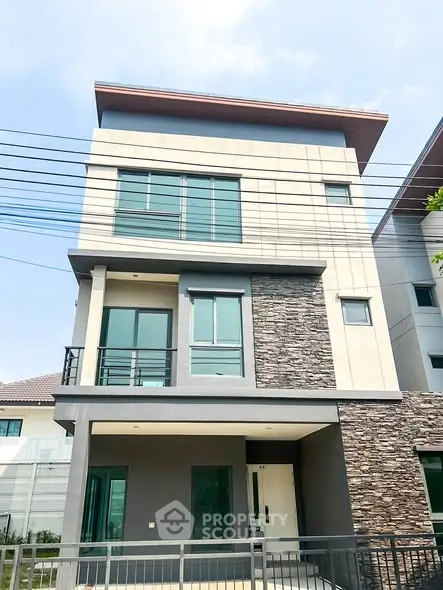 Modern three-story house with stone facade and large windows in a suburban neighborhood.
