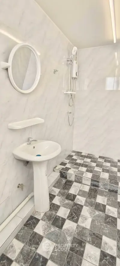 Modern bathroom with marble walls and checkered floor tiles, featuring a round mirror and sleek fixtures.