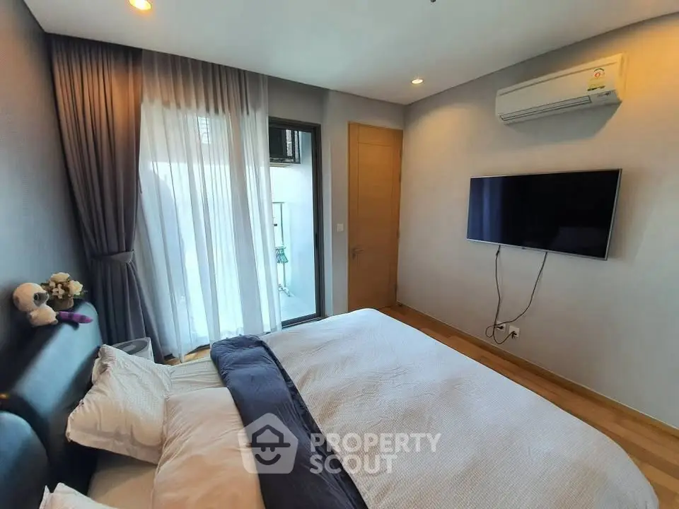 Modern bedroom with balcony access and wall-mounted TV in a stylish apartment.