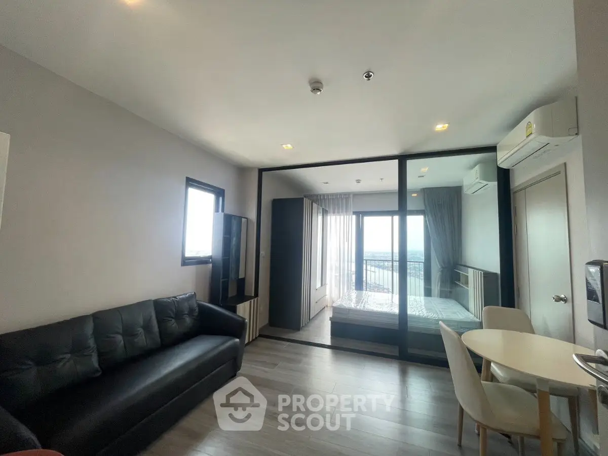 Modern apartment with open living room and bedroom, featuring sleek furniture and large windows.