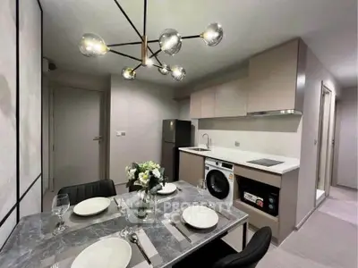 Modern kitchen with dining area, featuring sleek cabinetry, washing machine, and elegant lighting.