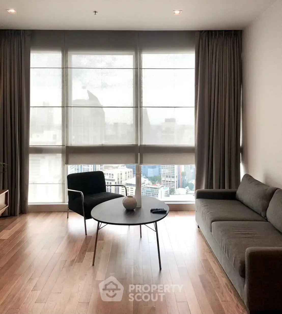 Modern living room with large windows and city view, featuring sleek furniture and wooden flooring.
