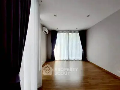 Spacious empty room with hardwood floors and large windows with curtains.