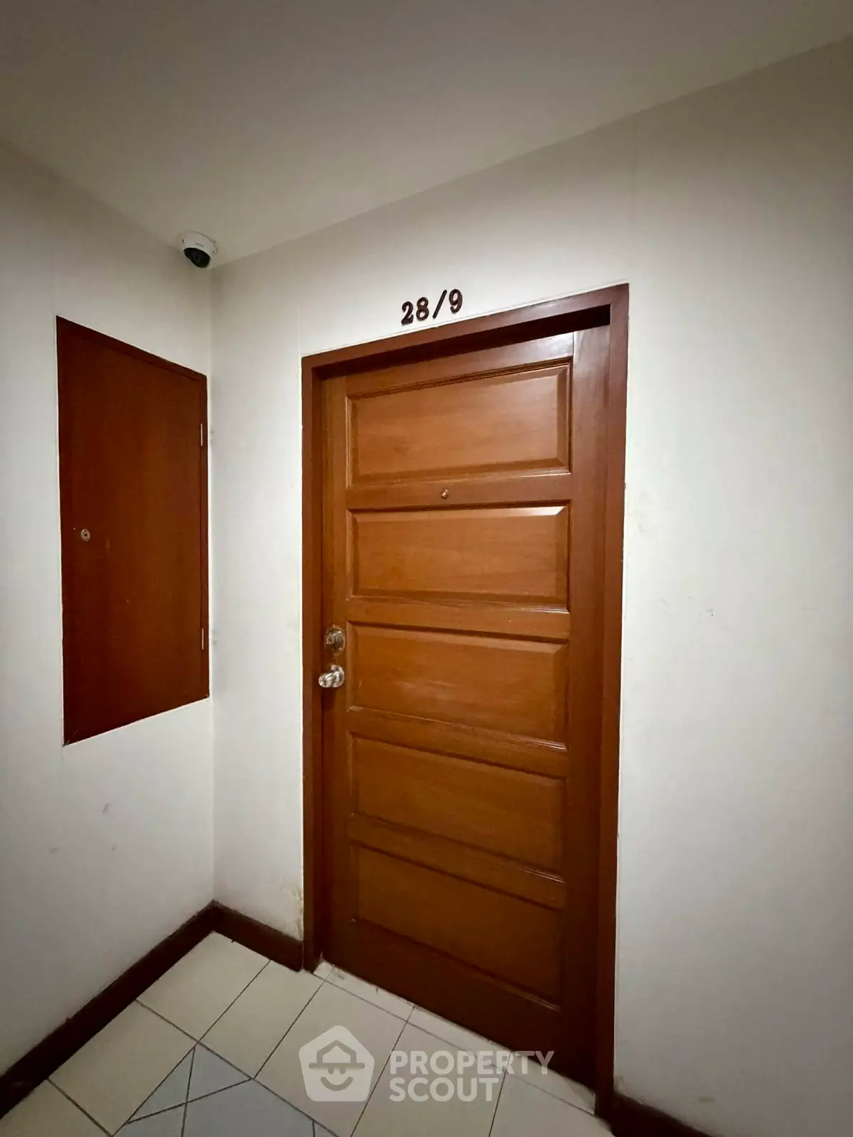 Secure apartment entrance with wooden door and surveillance camera for added safety.