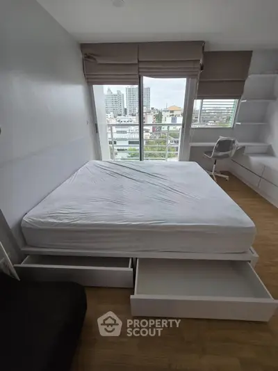 Modern bedroom with city view, featuring a bed with storage drawers and a sleek workspace.