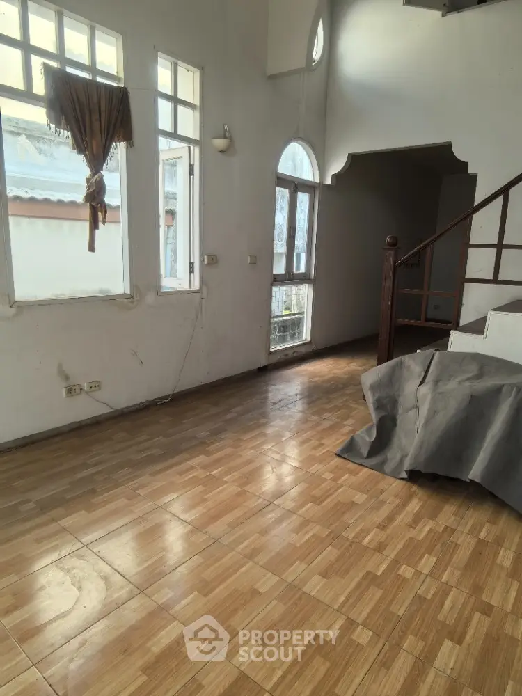 Spacious living room with large windows and wooden flooring, featuring a staircase and natural light.