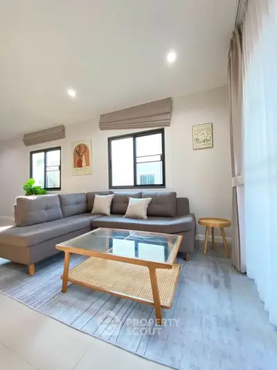 Modern living room with stylish gray sectional sofa, glass coffee table, and large windows for natural light.