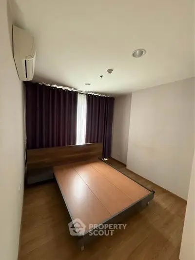 Spacious bedroom with wooden flooring and modern bed frame, featuring elegant curtains and air conditioning.