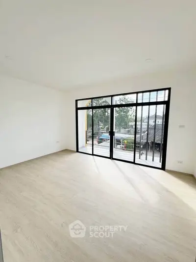 Spacious empty room with large windows and wooden flooring, offering abundant natural light and a modern aesthetic.