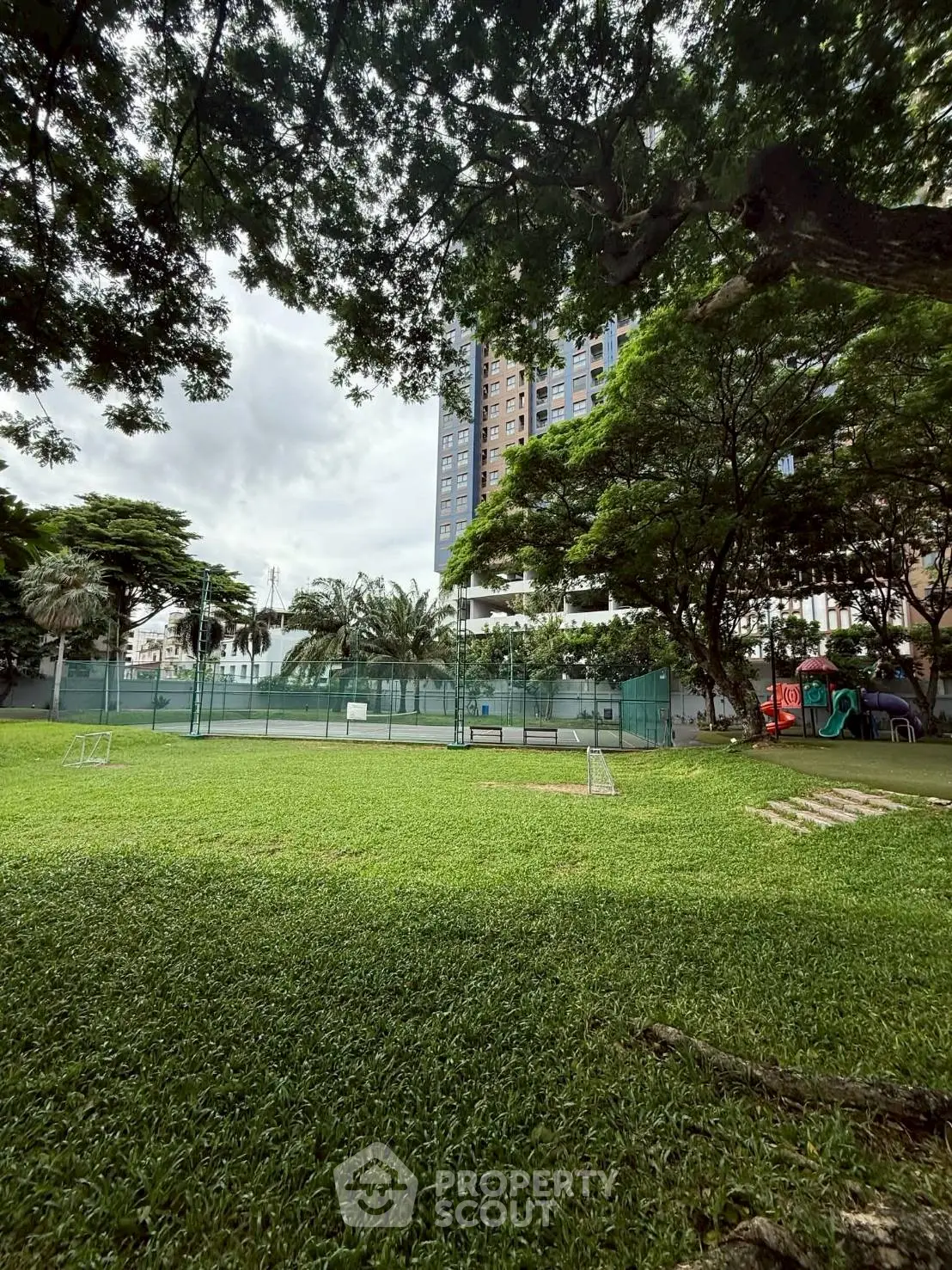 Lush green garden with tennis court and playground in modern residential complex.