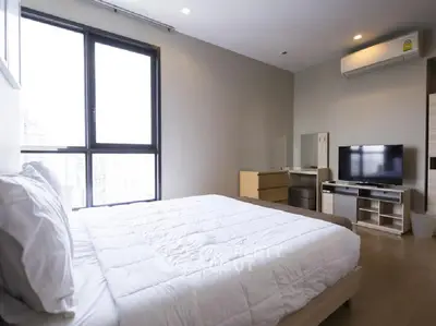 Modern bedroom with large window and sleek furnishings in a high-rise apartment.