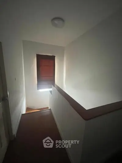 Dimly lit hallway with wooden flooring and a window casting soft light.