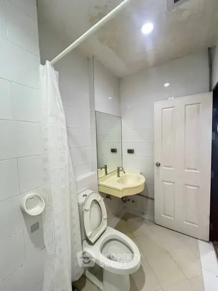 Compact bathroom with white tiles, toilet, and sink, ideal for small spaces.