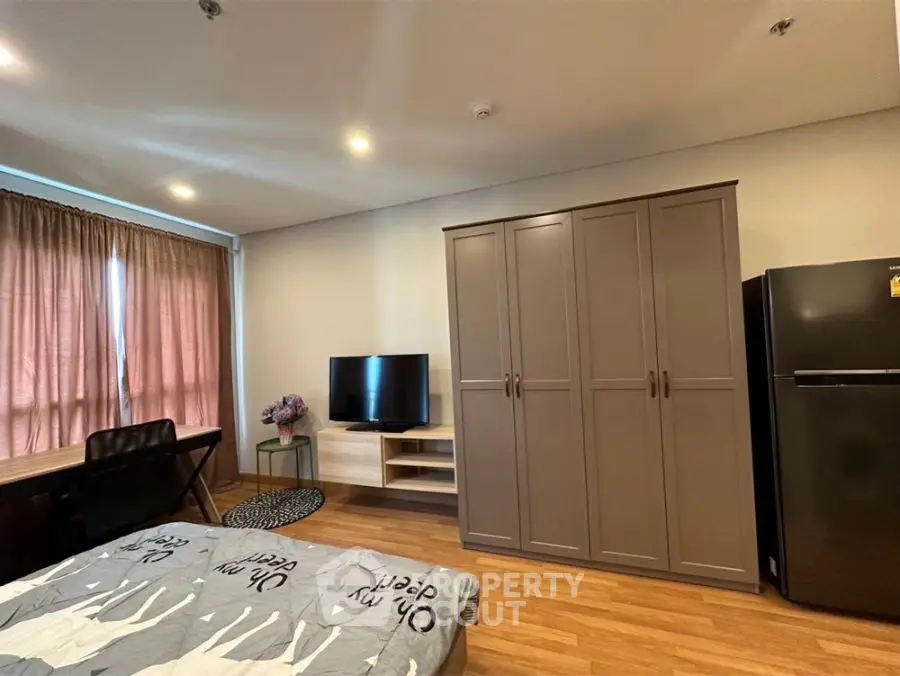 Modern bedroom with TV, wardrobe, and desk in cozy apartment setting.