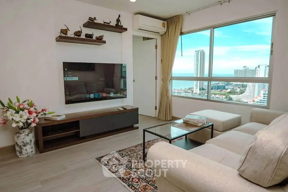Modern living room with large window offering stunning city and sea views, featuring cozy sofa and sleek TV setup.