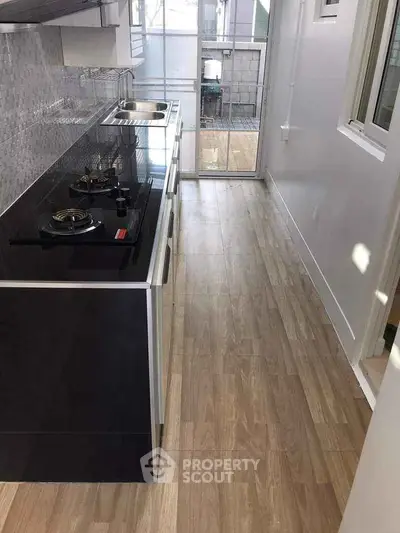 Modern kitchen with sleek black cabinetry and gas stove, featuring a bright open layout and wooden flooring.