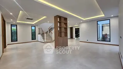 Spacious modern living room with elegant lighting and open layout, featuring a stylish staircase and large windows.