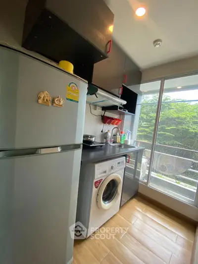 Modern kitchen with washing machine and fridge, featuring sleek cabinetry and large window view.