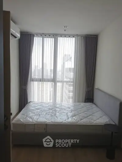 Modern bedroom with large window and city view, featuring a stylish bed and elegant curtains.