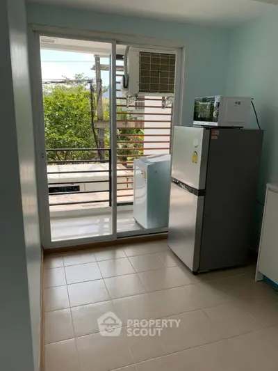 Compact kitchen with fridge and microwave, sliding door to balcony with greenery view.