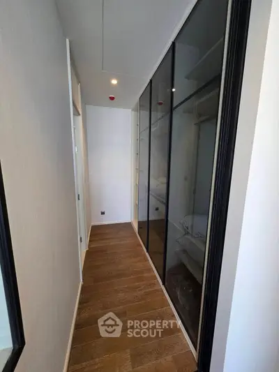 Modern hallway with sleek glass wardrobes and wooden flooring in a contemporary apartment.